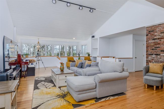 Living area featuring high vaulted ceiling, a healthy amount of sunlight, light wood finished floors, and a chandelier | Image 9