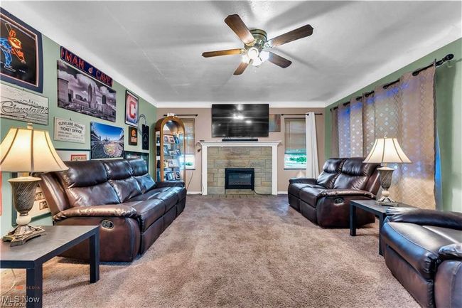 Living room with carpet floors, a ceiling fan, a stone fireplace, and baseboards | Image 5