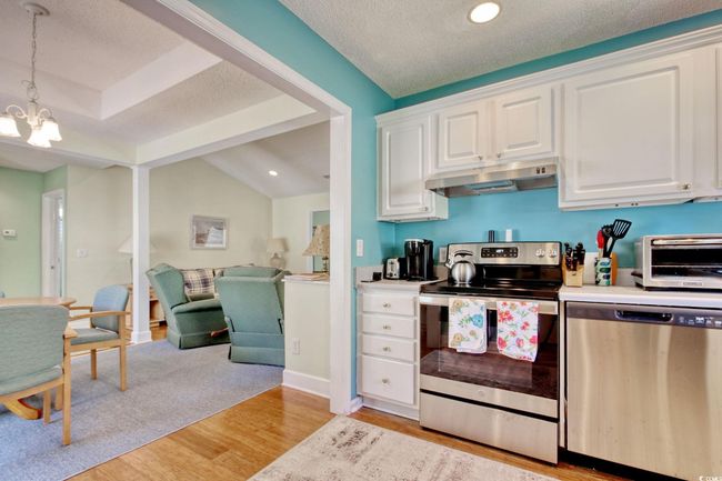 Kitchen with stainless steel appliances, under cabinet range hood, light wood-type flooring, a chandelier, and white cabinetry | Image 14