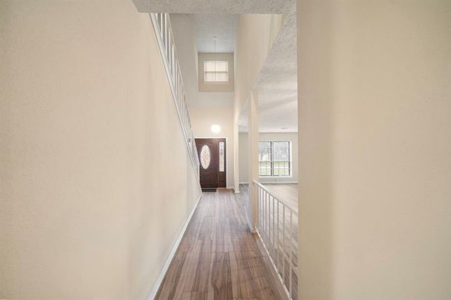 Step inside to a welcoming foyer highlighted by soaring ceilings and neutral tile flooring. The entry offers a direct view of the open living area and features a modern stair railing. | Image 7