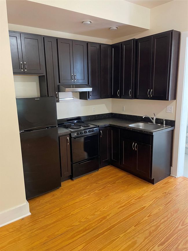 Kitchen with stove, fridge, range hood, dark countertops, and a sink | Image 5
