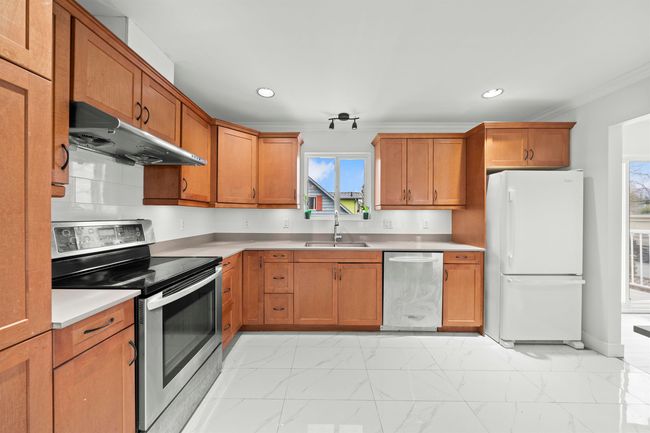 Kitchen featuring ornamental molding, under cabinet range hood, marble finish floor, a sink, and appliances with stainless steel finishes | Image 5