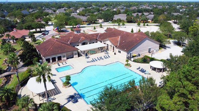 This aerial photo shows a spacious community clubhouse with a large outdoor swimming pool surrounded by lounge chairs, lush greenery and ample parking. Not shown, is the neighborhood's large, stocked pond with concrete walking trail encircling. | Image 31