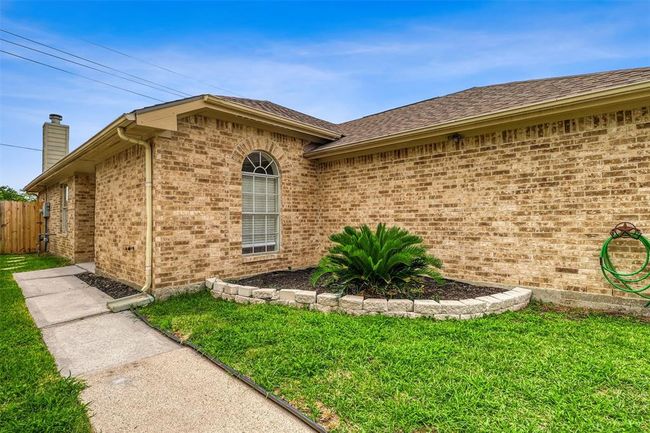 Follow the curved concrete walkway to the side-entry front door, where charming details like a stacked-stone flower bed and full gutters add both style and function to the home’s exterior. | Image 4