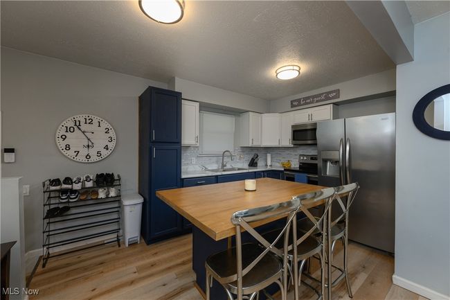 Kitchen with stainless steel appliances, wood counters, light wood-style flooring, decorative backsplash, and a kitchen bar | Image 7