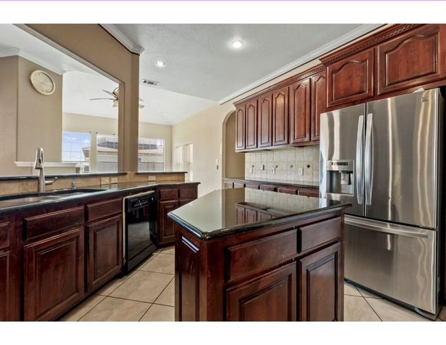 Kitchen with stainless steel fridge with ice dispenser, backsplash, light tile patterned flooring, ornamental molding, and a center island | Image 17