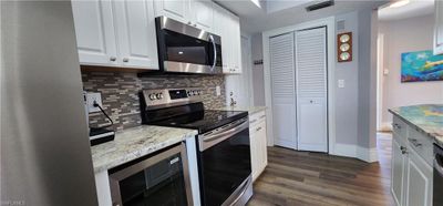 Kitchen featuring light stone countertops, dark wood-type flooring, appliances with stainless steel finishes, white cabinets, and backsplash | Image 3