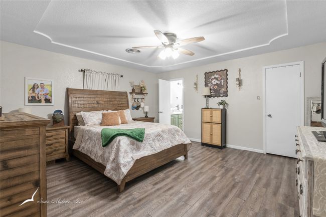 Bedroom featuring ceiling fan, a textured ceiling, wood finished floors, baseboards, and connected bathroom | Image 13
