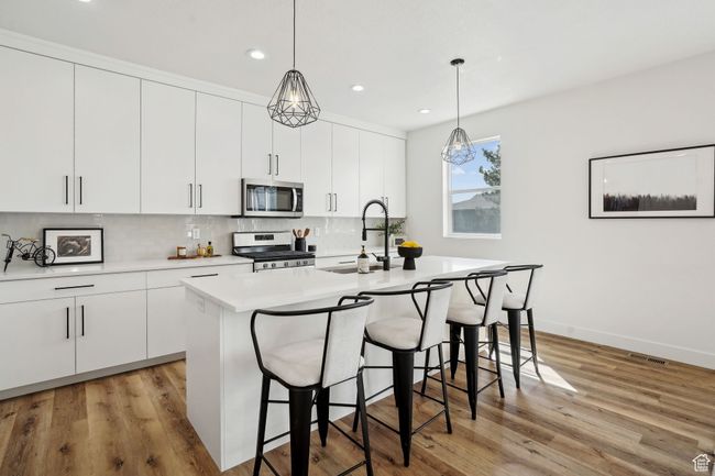 Kitchen with a kitchen breakfast bar, stainless steel appliances, light countertops, a sink, and tasteful backsplash | Image 9