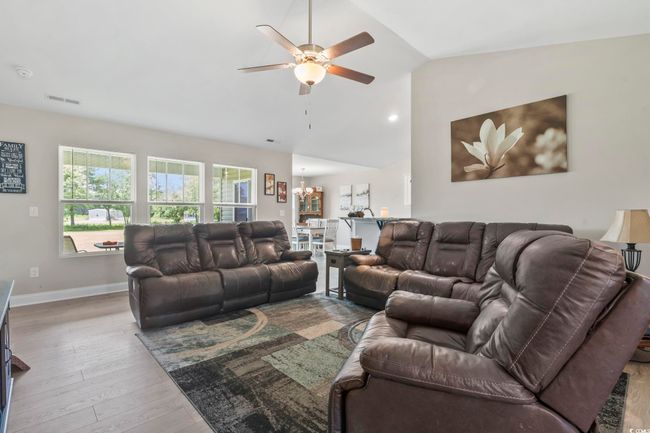 Living area featuring vaulted ceiling, a ceiling fan, wood finished floors, and a chandelier | Image 6