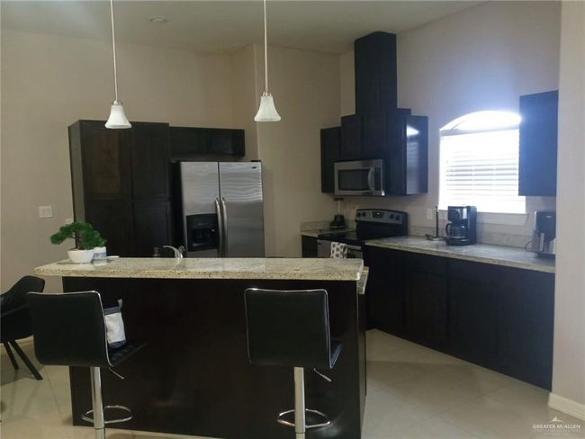 Kitchen featuring appliances with stainless steel finishes, dark cabinetry, a breakfast bar area, and hanging light fixtures | Image 4