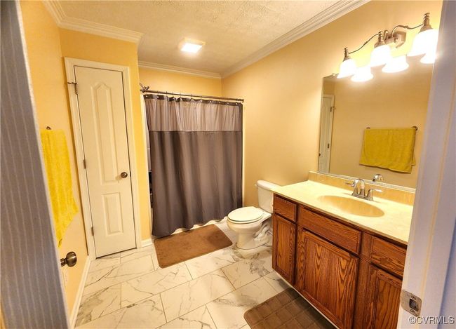 Full bathroom featuring marble look tile flooring, vanity, a shower with curtain, a textured ceiling, and crown molding | Image 25