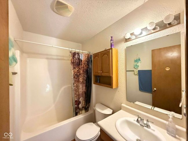 full bath featuring a textured wall, shower / bath combo with shower curtain, vanity, and a textured ceiling | Image 16
