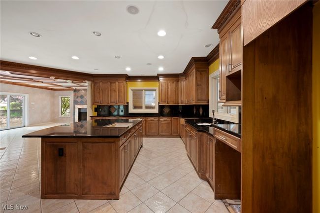 Kitchen with dark countertops, a kitchen island, backsplash, light tile patterned floors, and recessed lighting | Image 17