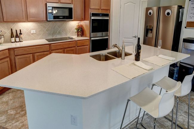 Kitchen featuring appliances with stainless steel finishes, a breakfast bar, tasteful backsplash, light countertops, and a center island with sink | Image 20