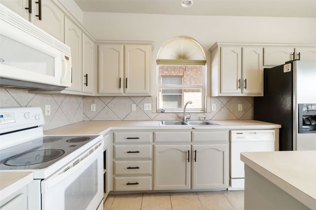 Kitchen with a sink, white appliances, light tile patterned floors, and light countertops | Image 19