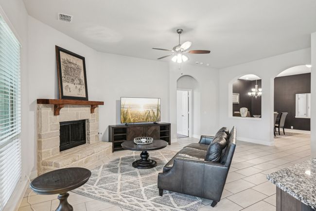Living room with arched walkways, ceiling fan, light tile patterned tile floors, a stone gas fireplace, and view formal dining or formal living | Image 13