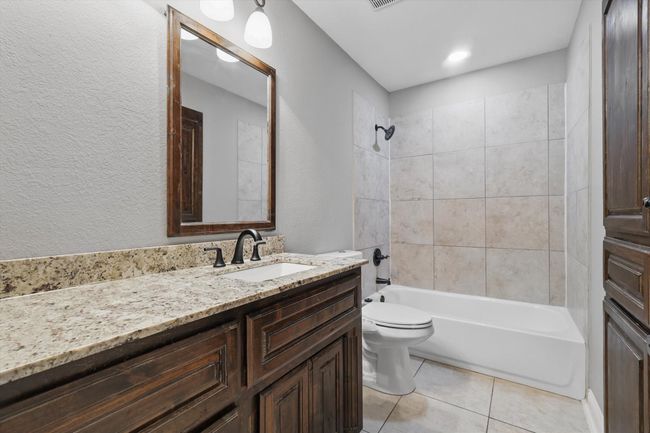 Bathroom with vanity, toilet, tile patterned flooring, tub / shower combination, and a textured wall | Image 25