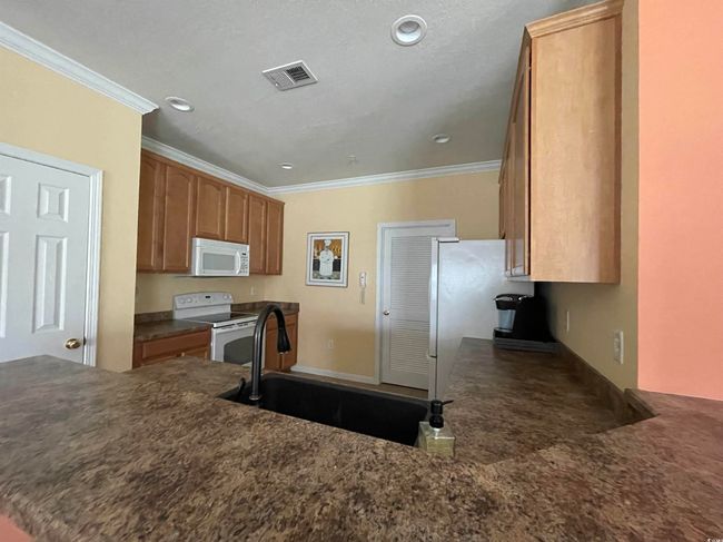 Kitchen featuring visible vents, crown molding, a peninsula, white appliances, and a sink | Image 13