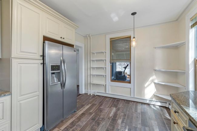 Kitchen featuring stainless steel fridge with ice dispenser, open shelves, dark wood-type flooring, a baseboard radiator, and crown molding | Image 17