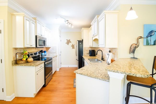 Kitchen featuring stainless steel appliances, a peninsula, a kitchen breakfast bar, light wood-style flooring, and decorative backsplash | Image 9