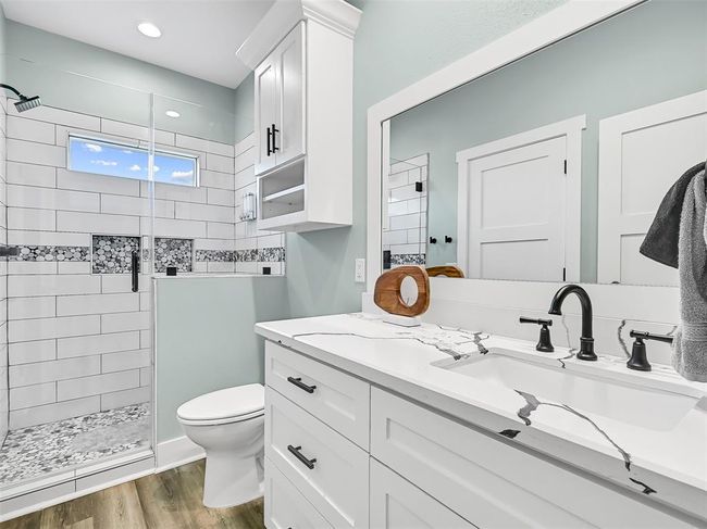 This functional and beautifully finished en suite bath boasts a quartz countertop vanity with a rectangular basin sink, stylish black fixtures, white cabinetry, and a custom tile walk-in shower with dual niches and frameless glass door. | Image 21