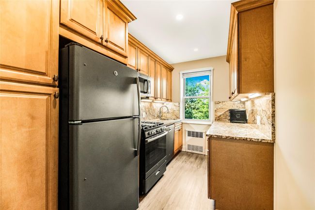 Kitchen with appliances with stainless steel finishes, radiator, light wood-style flooring, decorative backsplash, and light stone counters | Image 8