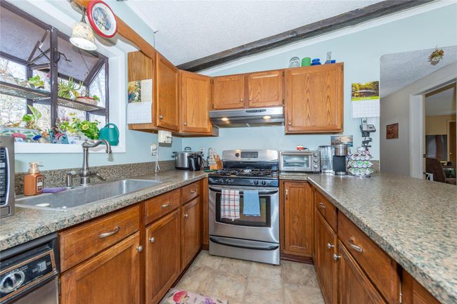 Kitchen with brown cabinets, a sink, a textured ceiling, gas range, and under cabinet range hood | Image 7