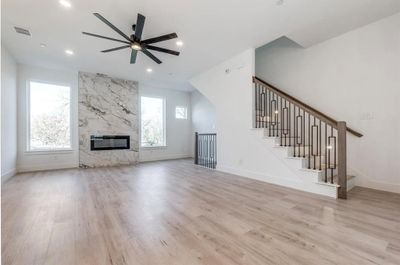 Unfurnished living room with light wood-type flooring, ceiling fan, and a fireplace | Image 2