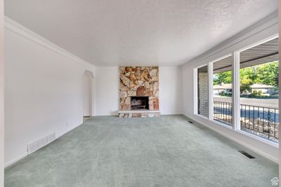 Living room with a textured ceiling, ornamental molding, carpeted floors, and a fireplace, large front windows | Image 2