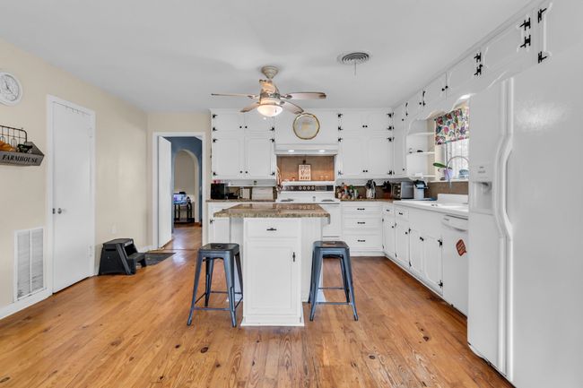 Kitchen featuring white appliances, arched walkways, a kitchen breakfast bar, open shelves, and white cabinetry | Image 12