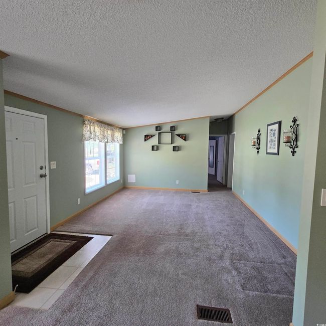Unfurnished living room featuring carpet flooring, a textured ceiling, crown molding, and tile patterned flooring | Image 14