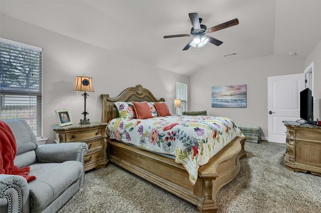 Bedroom with light colored carpet, vaulted ceiling, baseboards, ceiling fan, and visible vents | Image 18