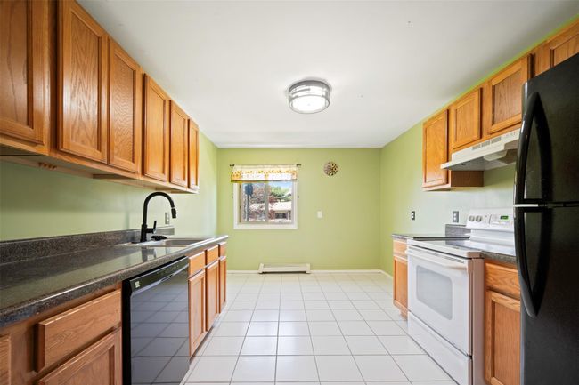 Kitchen featuring dark countertops, a sink, a baseboard radiator, black appliances, and under cabinet range hood | Image 4