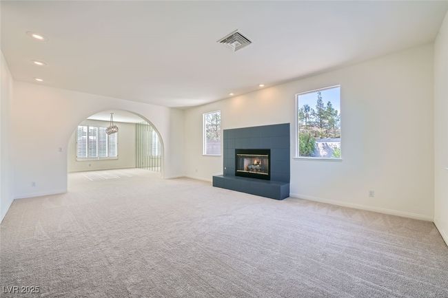 Unfurnished living room featuring arched walkways, a fireplace, visible vents, and light colored carpet | Image 22