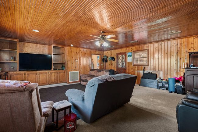 Living area featuring wooden walls, ceiling fan, dark colored carpet, and visible vents | Image 28
