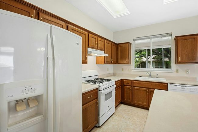 Kitchen with white appliances, under cabinet range hood, a sink, brown cabinets, and light countertops | Image 11