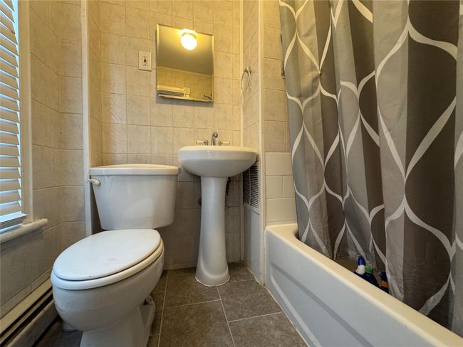 Full bathroom with tile walls, shower / bath combo with shower curtain, tile patterned floors, and a baseboard heating unit | Image 6
