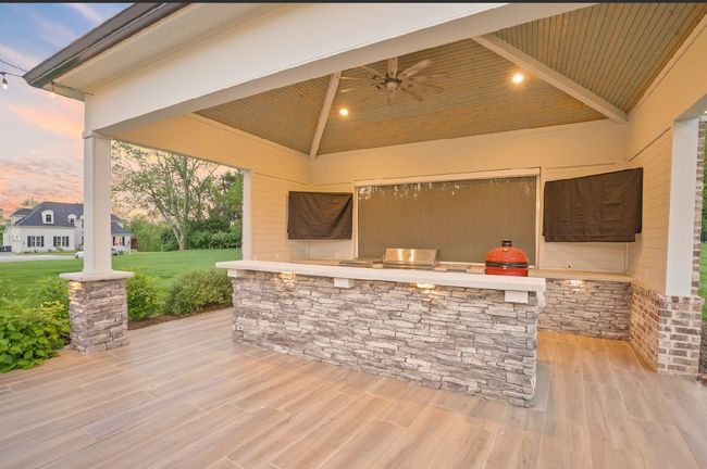 Sleek & fully equipped, this outdoor kitchen boasts stone finishes, a Kamado smoker, built-in grill, two mounted TVs, and a retractable patio shade—perfect for game days, cookouts, and relaxing in comfort, rain or shine. | Image 8