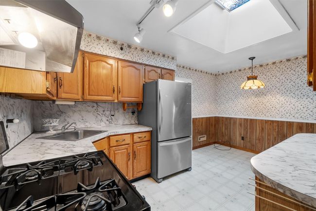 Kitchen with wainscoting, freestanding refrigerator, light countertops, light floors, and a sink | Image 14