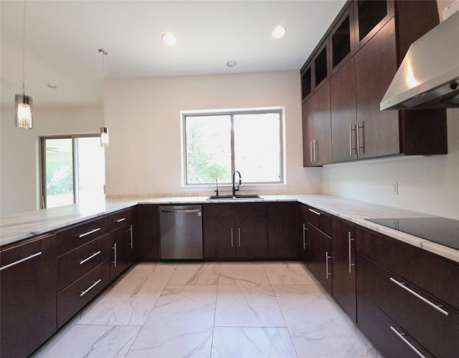 Kitchen with dishwasher, wall chimney exhaust hood, a sink, light marble finish flooring, and healthy amount of natural light | Image 6