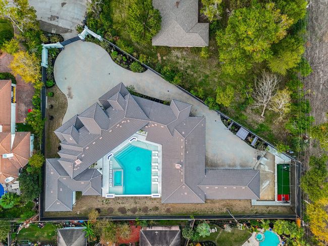 Aerial view of the home featuring a large central swimming pool. The property is surrounded by lush greenery and has a sizable gated driveway, offering privacy and ample outdoor space. | Image 7