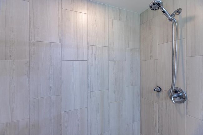 Marvel at the neutral-toned floor-to-ceiling marbled tile that wraps around the primary bathroom's | Image 18