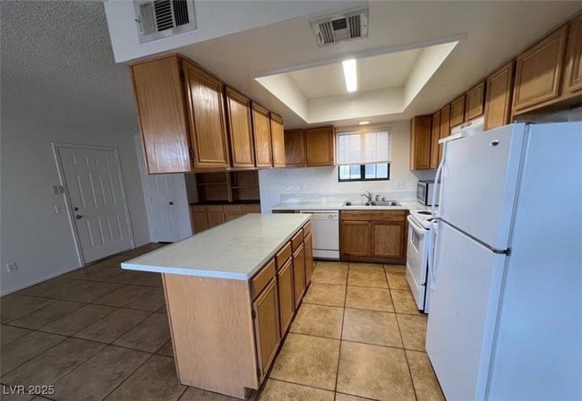Kitchen featuring white appliances, a sink, a tray ceiling, light countertops, and light tile patterned floors | Image 5