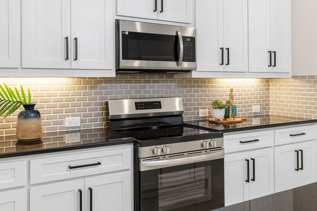 Kitchen with stainless steel appliances, white cabinets, decorative backsplash, and dark stone counters | Image 7