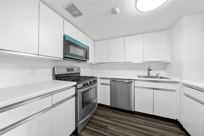 Kitchen featuring stainless steel appliances, a sink, light countertops, white cabinetry, and dark wood finished floors | Image 10