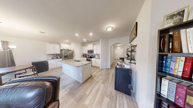 Kitchen featuring stainless steel appliances, arched walkways, light wood finished floors, white cabinetry, and an island with sink | Image 15
