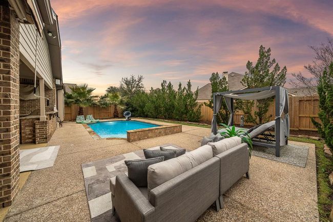 Outside, the lush backyard oasis creates a tropical paradise with mature landscaping providing a wall of privacy, a sparkling pool, and an outdoor kitchen—ideal for Texas summers. | Image 6