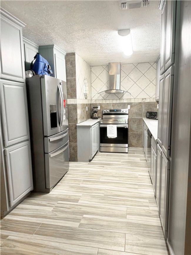 Kitchen featuring a textured ceiling, wall chimney exhaust hood, appliances with stainless steel finishes, and visible vents | Image 15