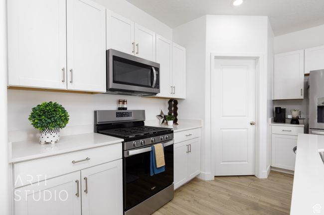 Kitchen with light wood finished floors, white cabinetry, stainless steel appliances, and light countertops | Image 13